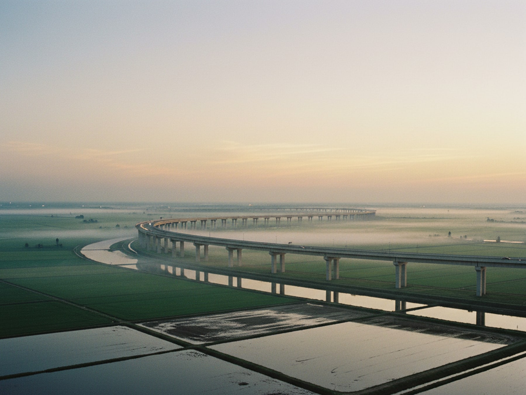 Long elevated expressway curving through green delta landscape at first light